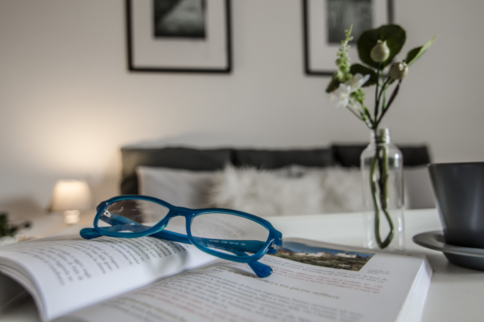 Home staging Dettaglio emozionale con occhiali libro vasetto di fiori e sullo sfondo letto accogliente